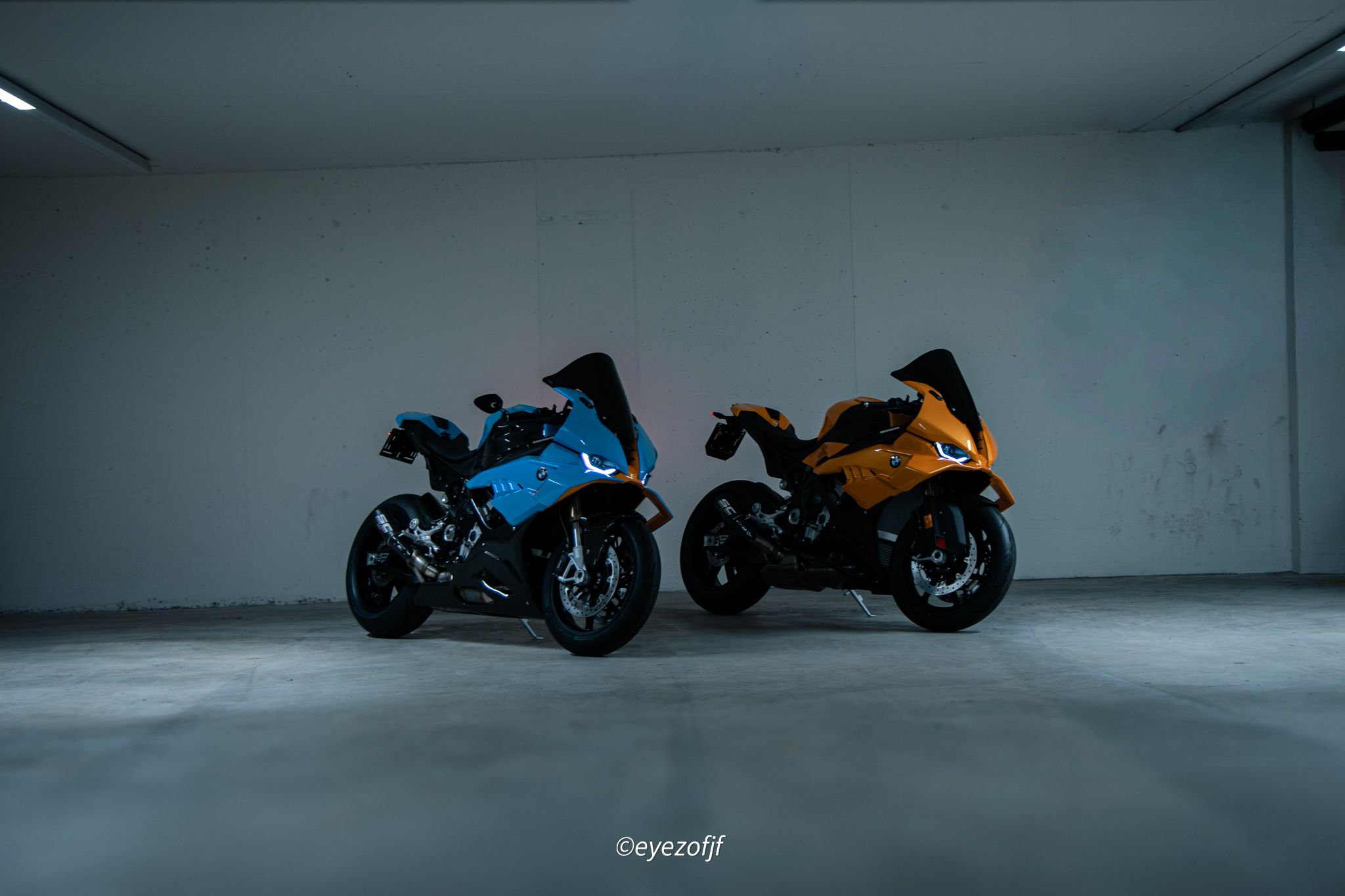 Zwei BMW-Sportmotorräder, blau und orange, in einer Tiefgarage